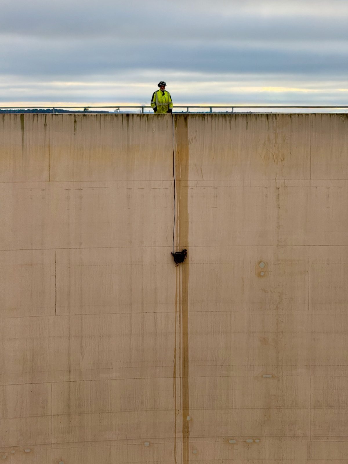Inspector on the tank rim with a scanning crawler on the shell wall